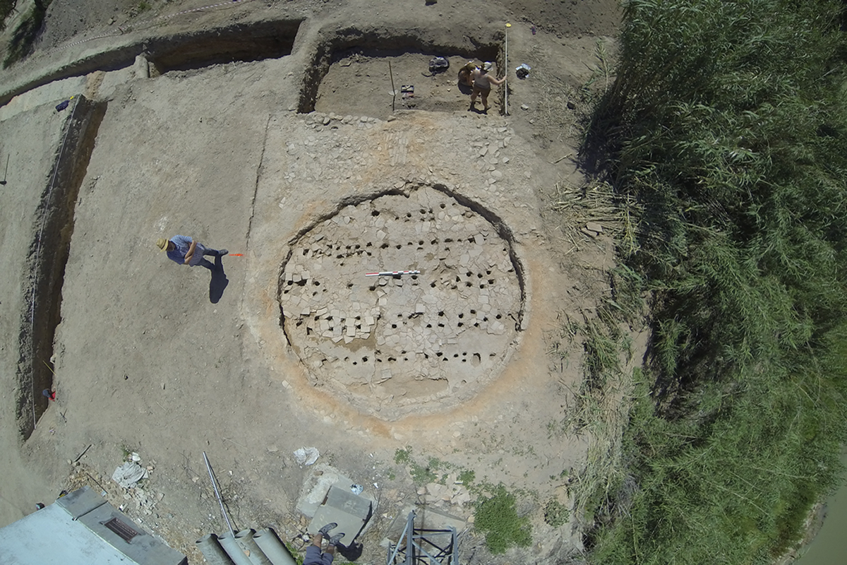 Horno 2 de Las Delicias, &Eacute;cija. Vista cenital
De los tres hornos circulares localizados en las excavaciones del alfar romano de Las Delicias, dos de ellos (hornos 2 y 3, excavados en 2014-2015) son de gran tama&ntilde;o (en torno a cinco metros de di&aacute;metro) mientras que el tercero (horno 1, excavado en 1997), era de tama&ntilde;o medio, con unos 3 metros de di&aacute;metro. Todos se fechan en la &uacute;ltima fase del alfar, datada en la primera mitad el siglo III d. C. En la fotograf&iacute;a cenital del horno 2, tomada en la campa&ntilde;a de 2014, se observa la parrilla que separa las c&aacute;maras de combusti&oacute;n y cocci&oacute;n (laboratorium) y el pasillo de alimentaci&oacute;n (praefurnium) de la primera de &eacute;stas.&nbsp;